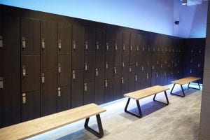 Locker room viewed from left. Laminate lockers with keyless 1 locks, three benches, and blue lights coming from the back.