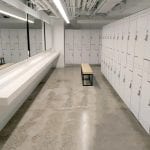Locker room. White shelf, and mirrors to the left, white "Z" shaped lockers in the back and right, and bench in the middle.