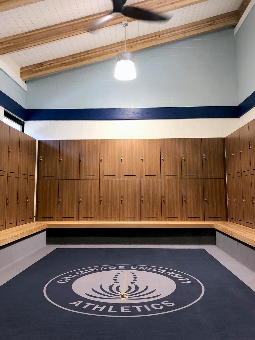 Room surrounded by phenolic lockers with Integrated Bench and blue rug with Chaminade University logo.