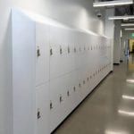 Hallway viewed from left with row of two-tier slope top white laminate lockers.